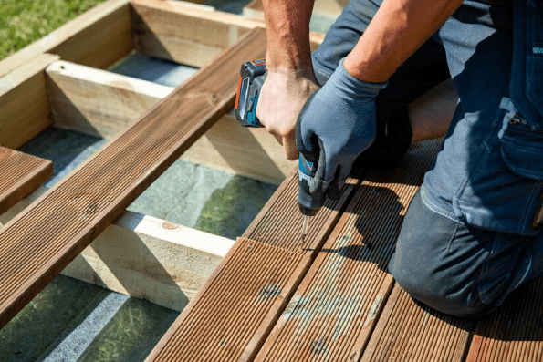 Deck construction builder hand with electric screwdriver installing impregnated wooden boards